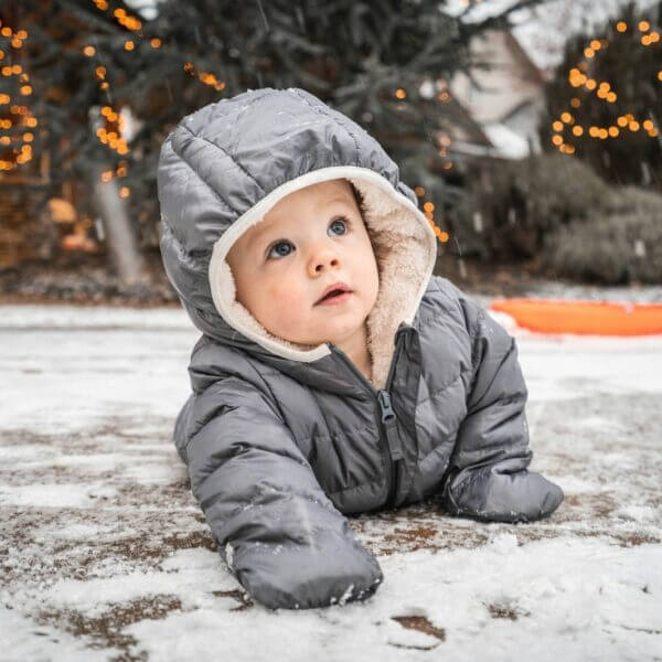 child in gray winter jacket lying on snow covered ground